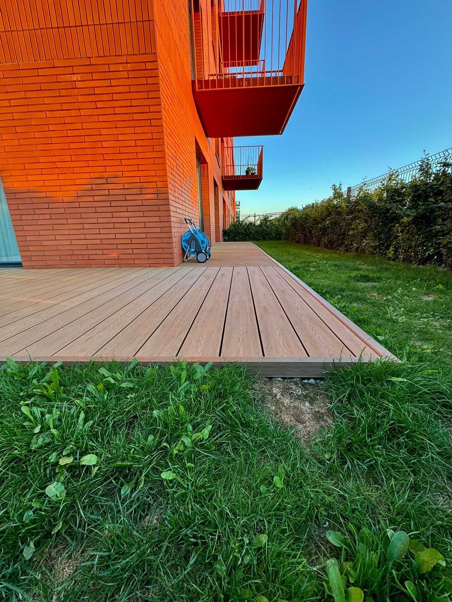 Taras L-shape przy narożniku apartamentowca z czerwonej cegły, ujęcie szerokie o złotej godzinie